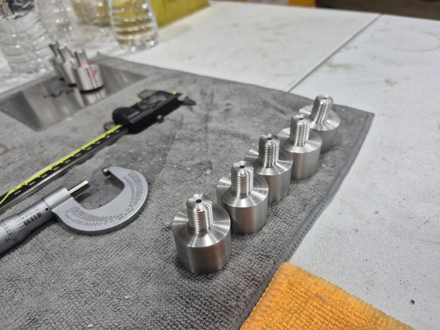 Row of small precision-turned stainless components with measuring tools