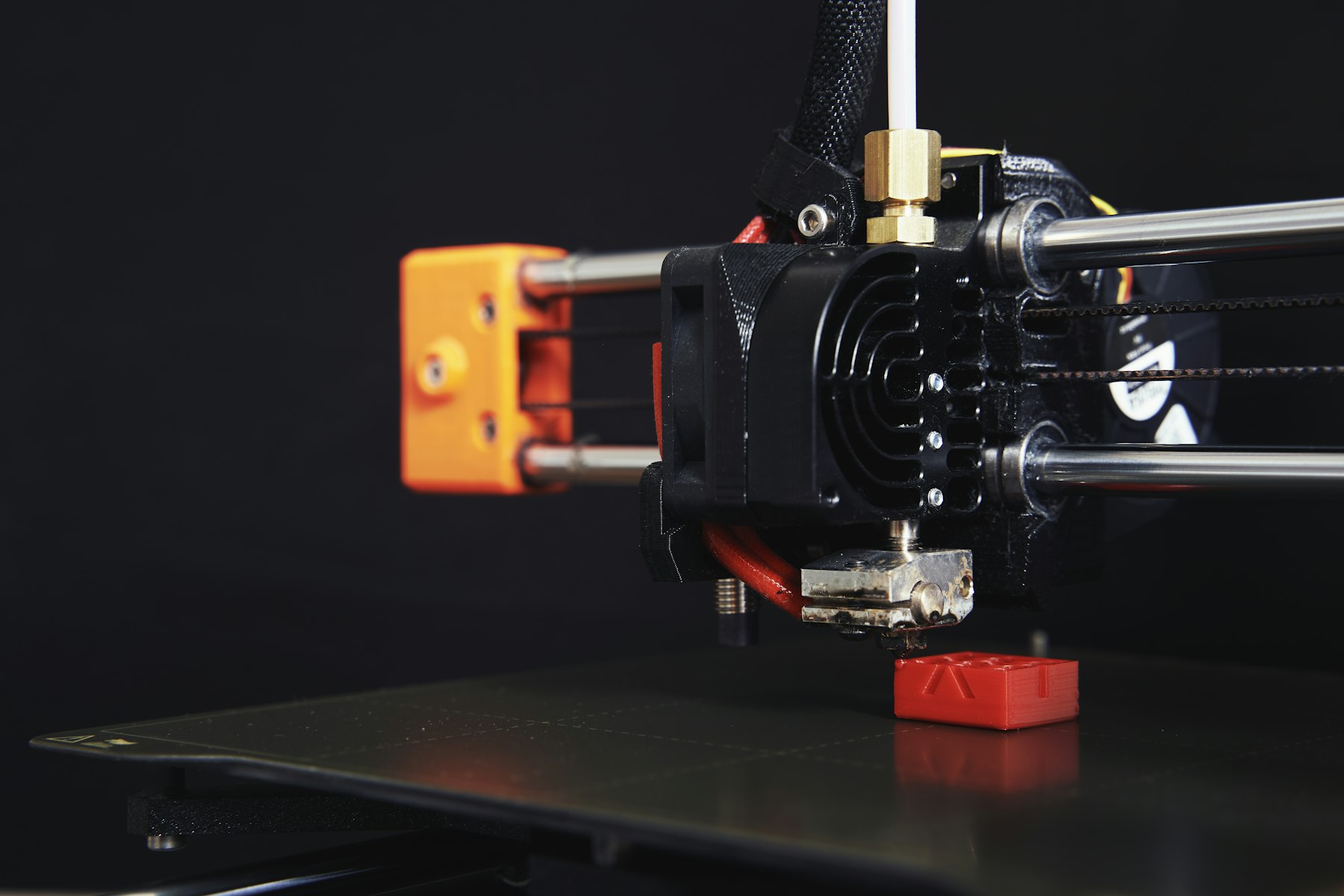 Close-up of a 3D printer nozzle laying down a red part