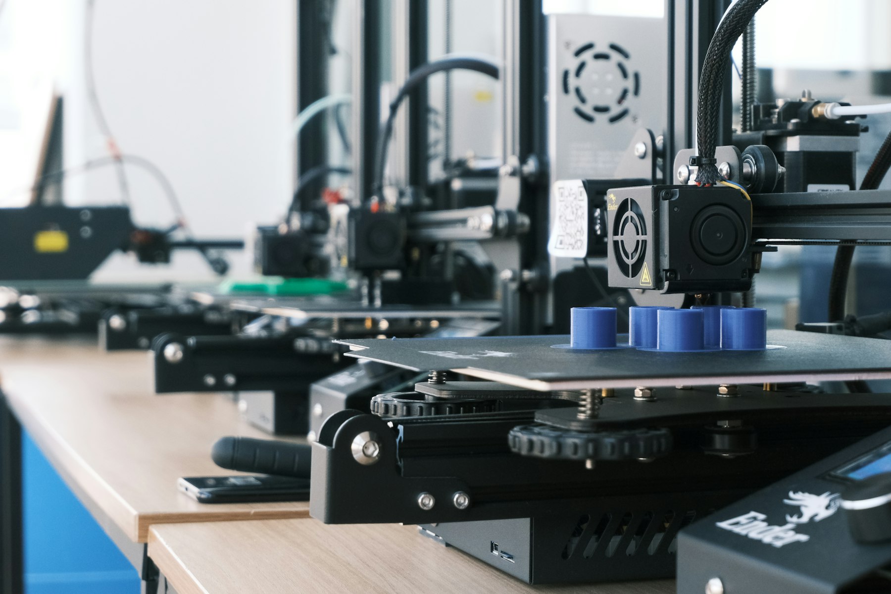 Row of desktop 3D printers producing blue plastic parts
