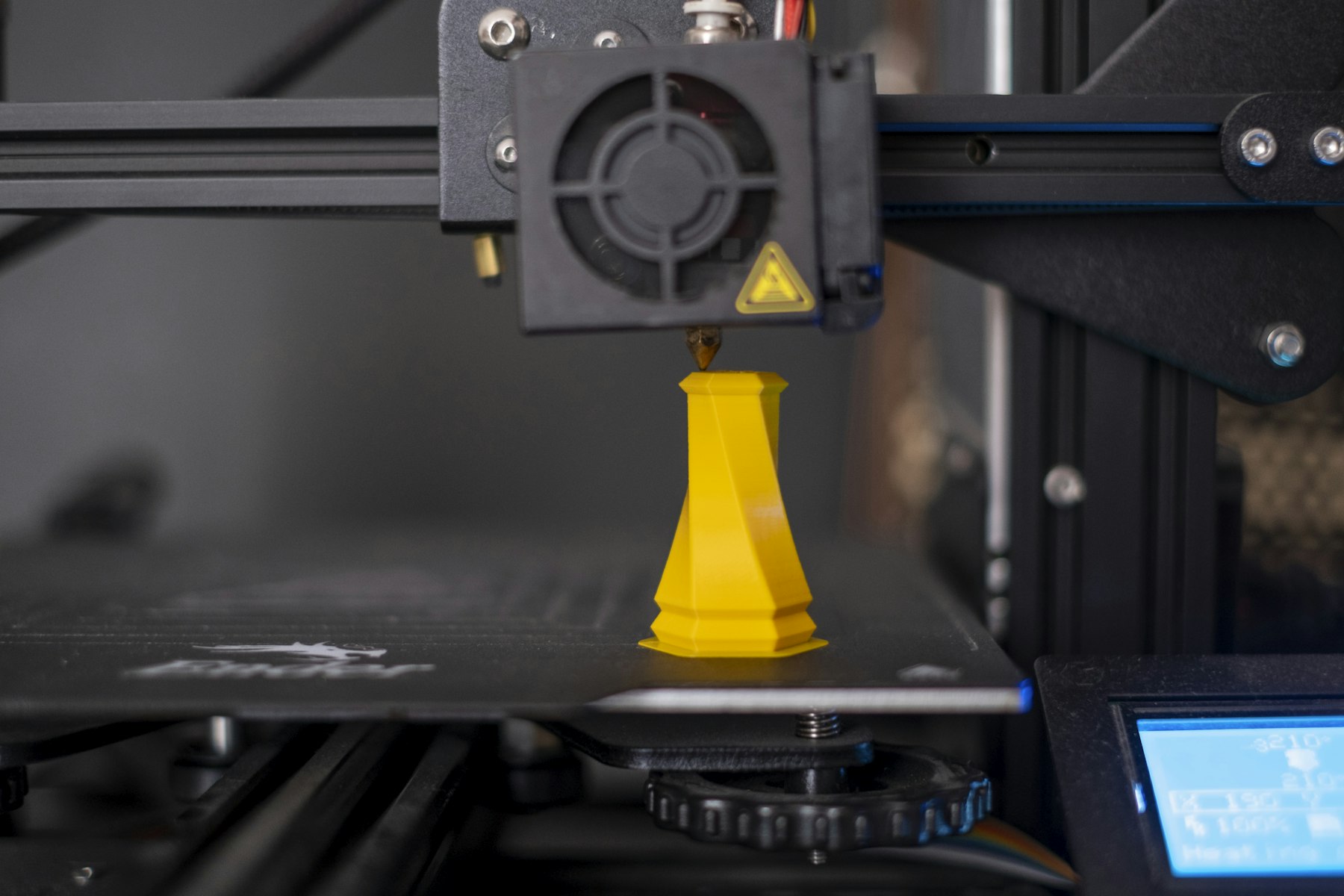 Desktop 3D printer extruding a yellow plastic part