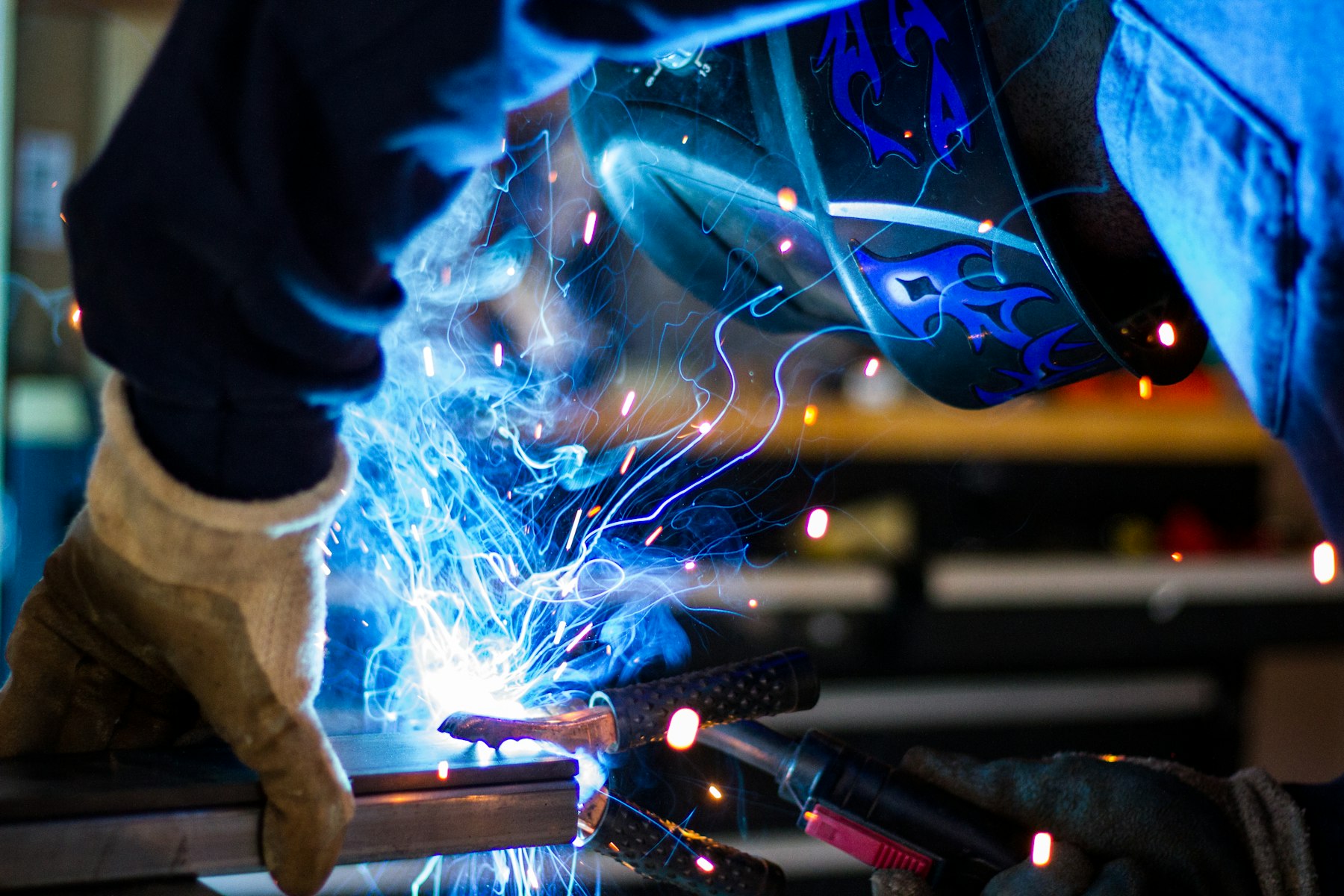 Welder in a protective helmet and gloves welding steel with sparks flying