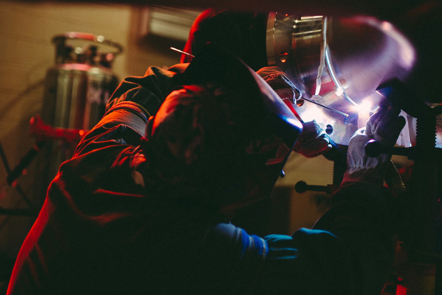 Welder in a protective helmet TIG welding a steel workpiece